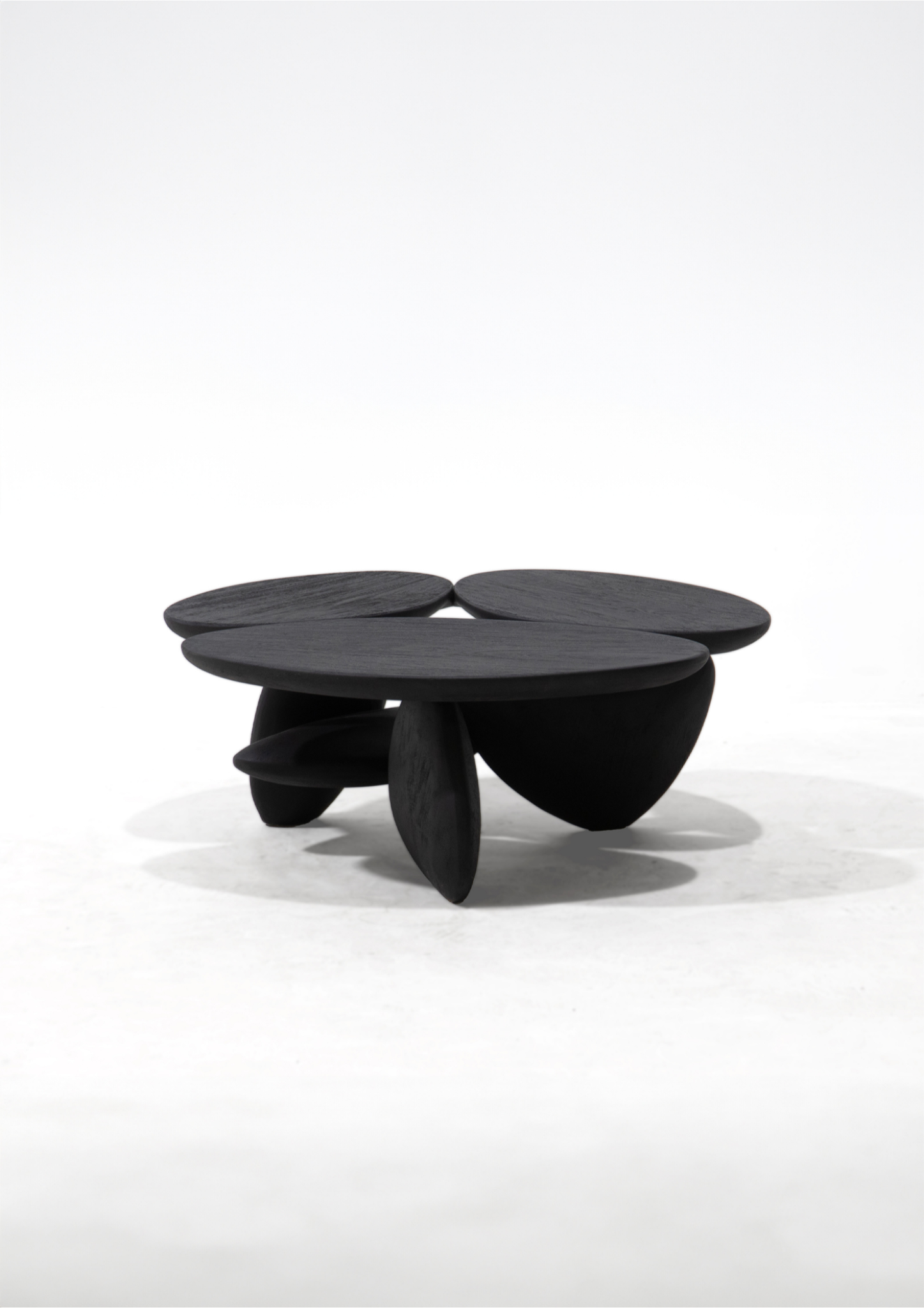 A modern black sculptural coffee table with a rounded, organic shape and three distinct pedestal legs, photographed on a seamless white studio background.