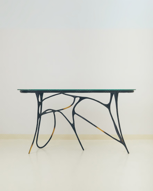 Black brass luxury handmade furniture table with organic design and glass top, perfect for modern luxury decor, on a light wooden floor with white wall background.