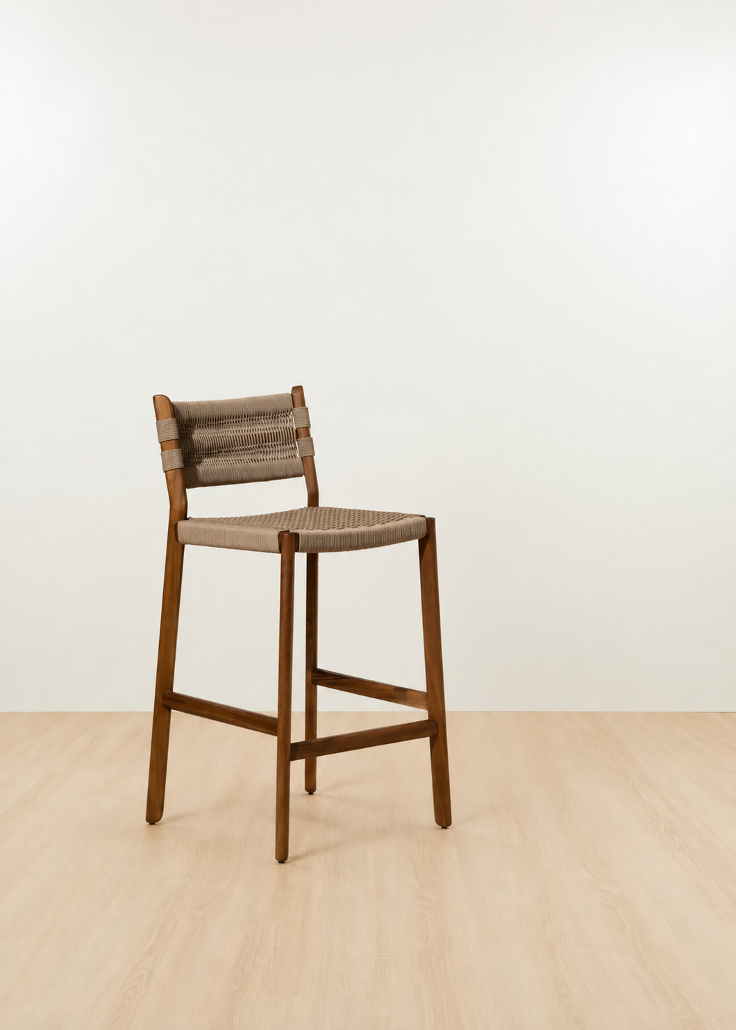 A wooden bar stool with a woven rope seat and backrest, positioned on a light wood floor against a plain off-white wall.