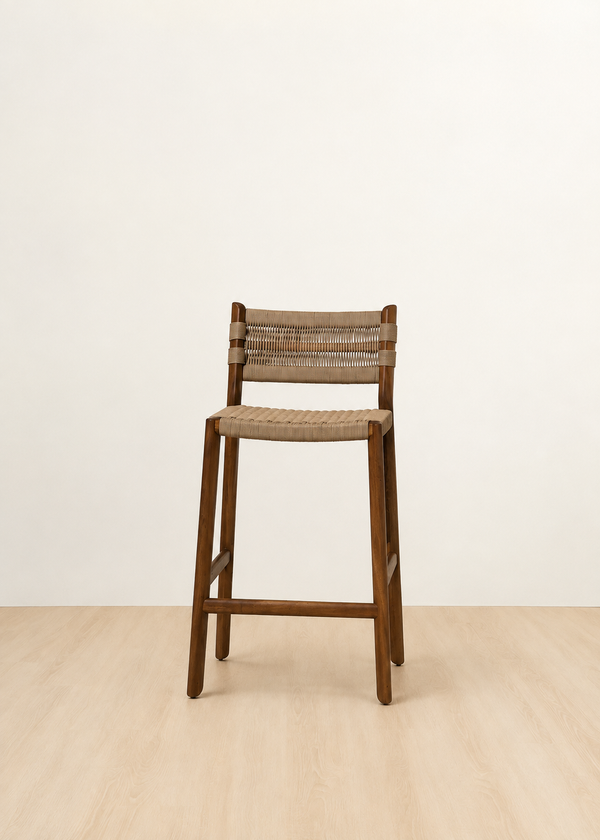 A wooden bar stool with a woven seat and backrest, shown in a minimalist studio setting with a light beige wall and pale wood floor.