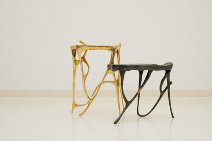 Two luxury handmade furniture stools, one gold brass and one black, designed for modern luxury decor, on a white background.