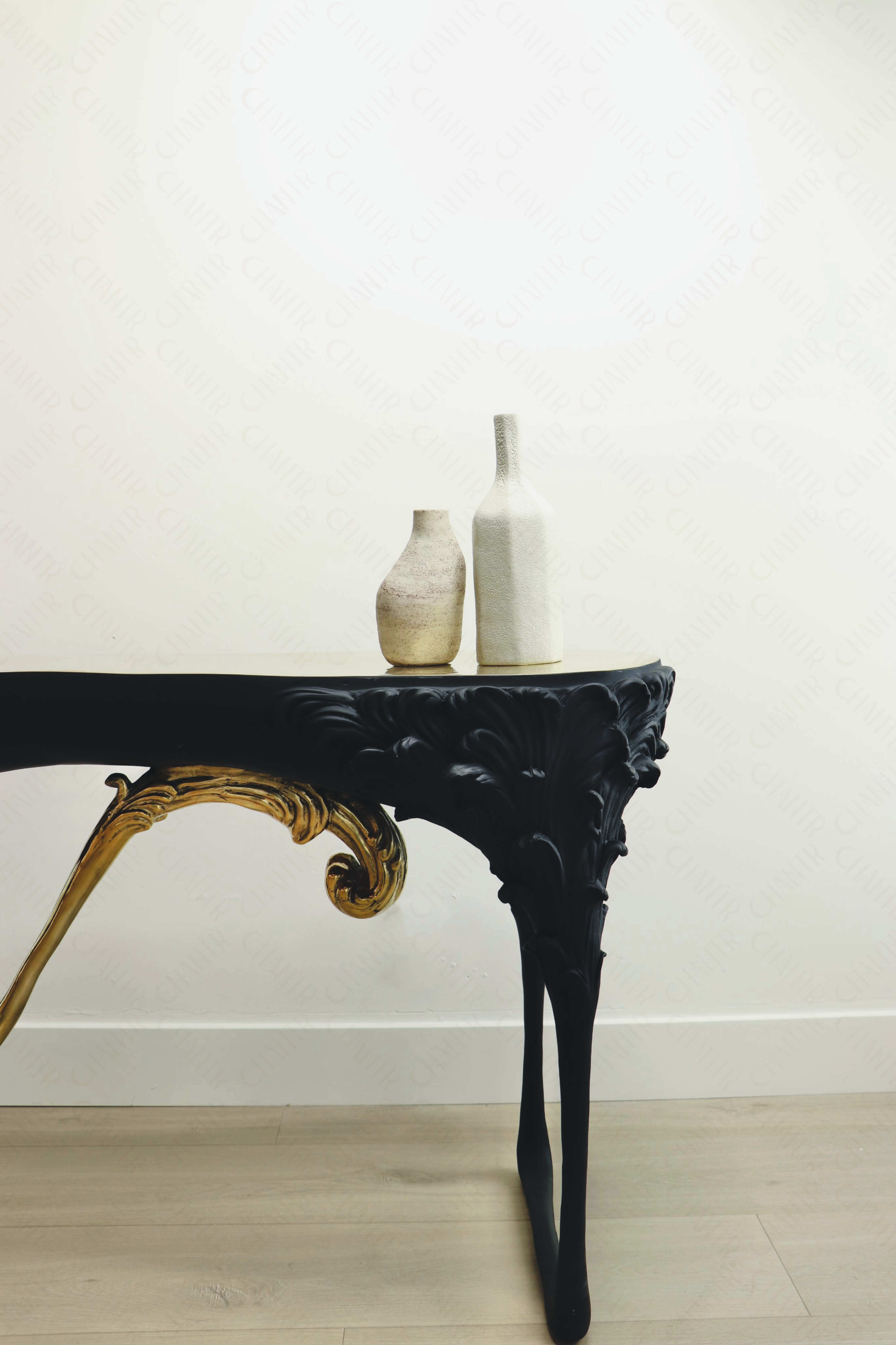 Zoomed in - Black console table with gold brass accents, luxury handmade furniture, styled with two vases, perfect for modern luxury decor, against a white wall.