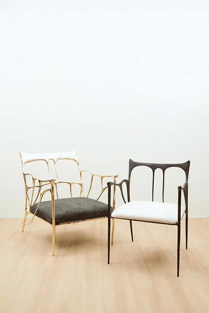 Two chairs, one with gold frame and black cushion, the other with black frame and white cushion, on a light wooden floor. Luxury handmade furniture