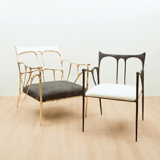 Two chairs, one with gold frame and black cushion, the other with black frame and white cushion, on a light wooden floor. Luxury handmade furniture
