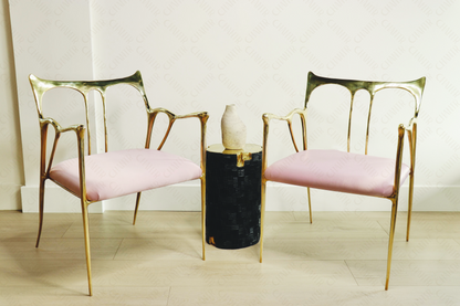 Two gold brass luxury handmade furniture chairs with pink cushions flanking a black and gold brass stool with a vase, perfect for modern luxury decor.