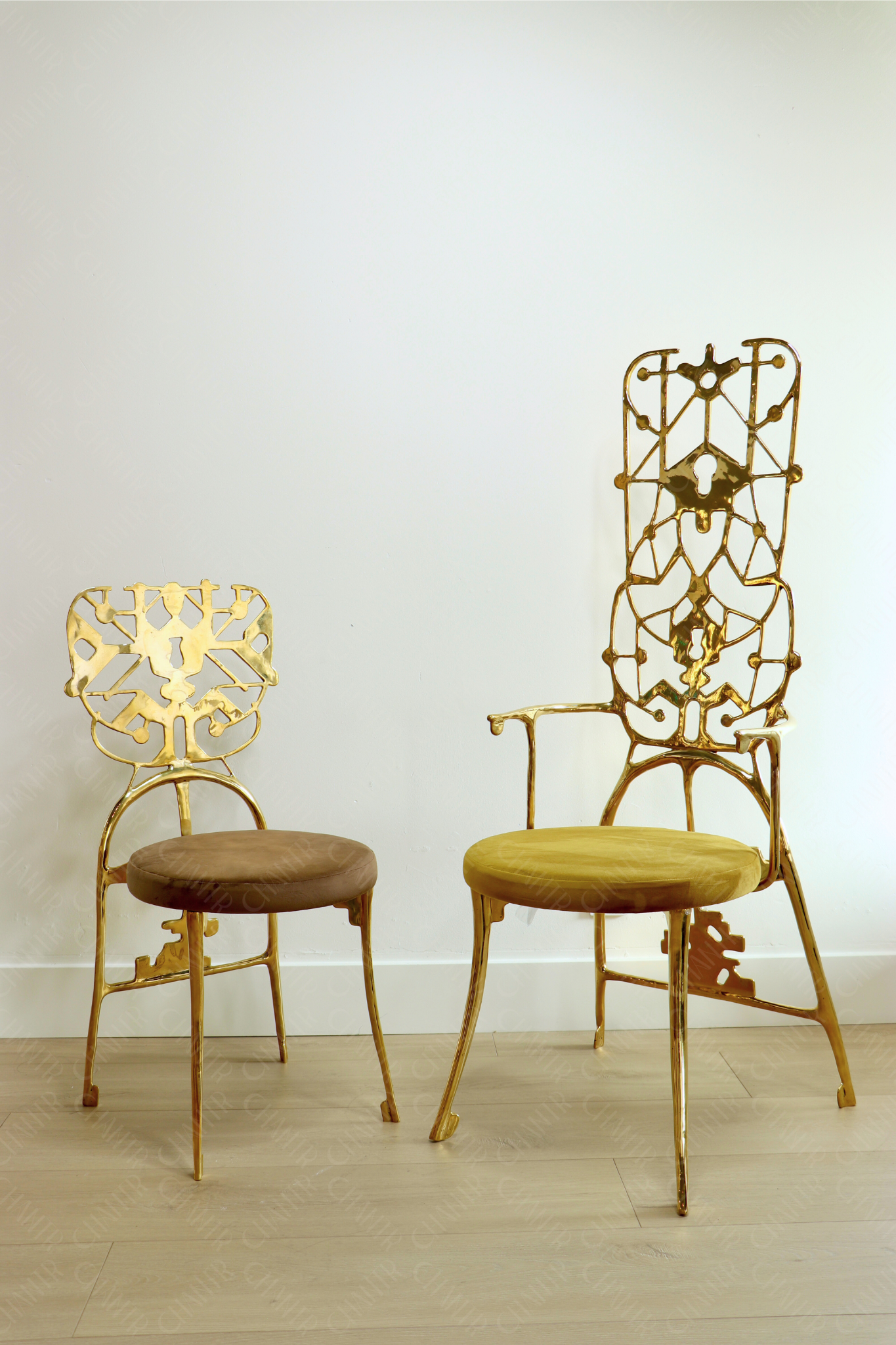 Two ornate gold chairs with intricate designs on a plain background. Luxury handmade furniture.
