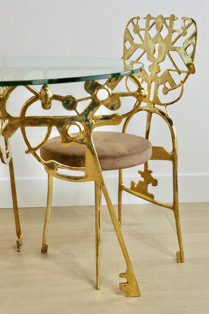 Gold dining chair with intricate design and glass table on a light wooden floor. Luxury handmade furniture