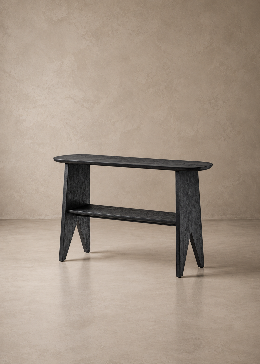 A modern black wooden console table with a rounded rectangular top, open lower shelf, and angled legs, set against a textured beige wall and concrete floor.