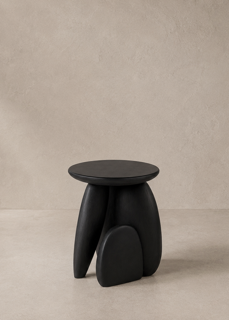 A modern black stool with a round seat and sculptural organic legs, set against a minimalist textured beige wall and floor.